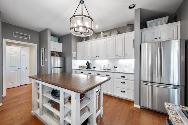 kitchen with white cabinets, hanging light fixtures, stainless steel fridge, and a notable chandelier