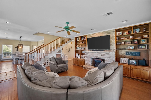 living room featuring ceiling fan, built in shelves, light wood-type flooring, and a fireplace