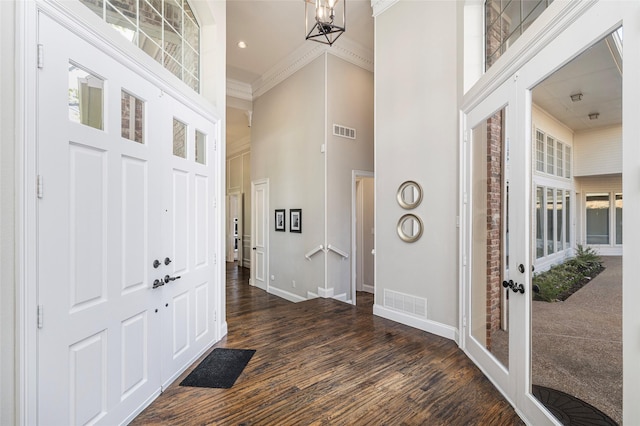 entrance foyer featuring a towering ceiling, dark hardwood / wood-style flooring, crown molding, and a chandelier