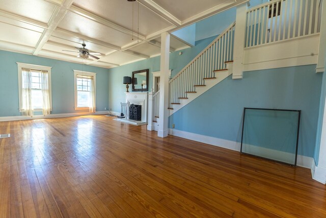 unfurnished living room featuring baseboards, coffered ceiling, a fireplace with raised hearth, ceiling fan, and wood-type flooring