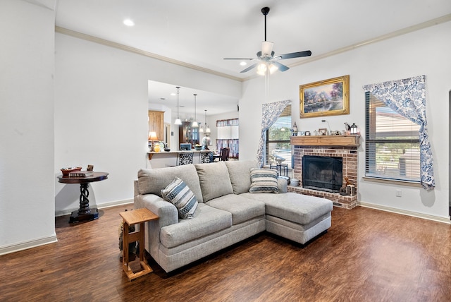 living room featuring a brick fireplace, ceiling fan, plenty of natural light, dark wood-type flooring, and crown molding