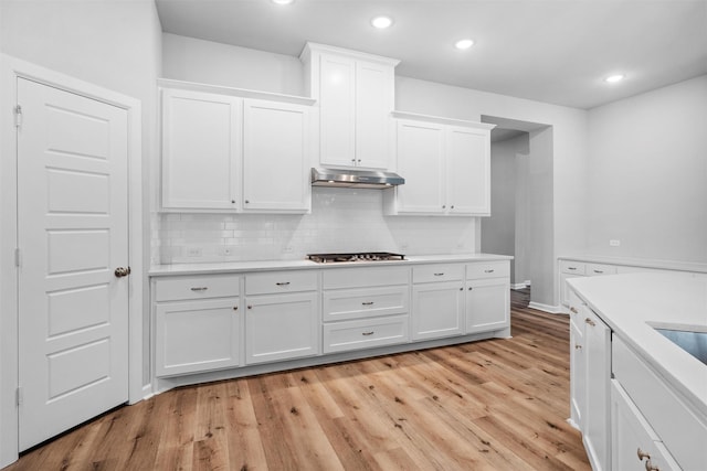 kitchen with under cabinet range hood, stainless steel gas stovetop, light countertops, and white cabinetry