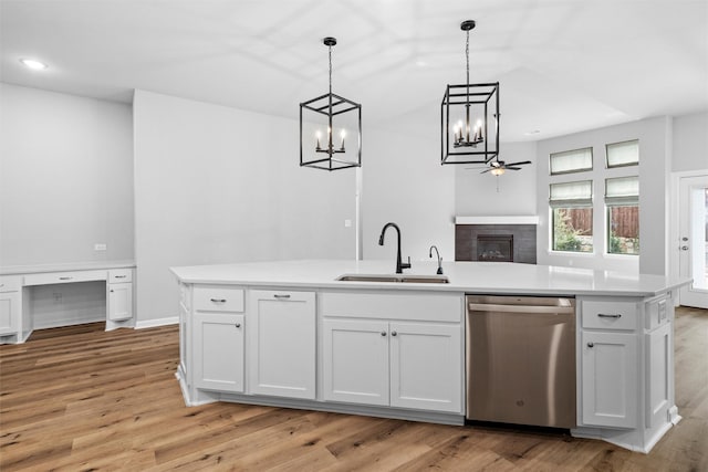 kitchen with a sink, white cabinetry, stainless steel dishwasher, and a tile fireplace