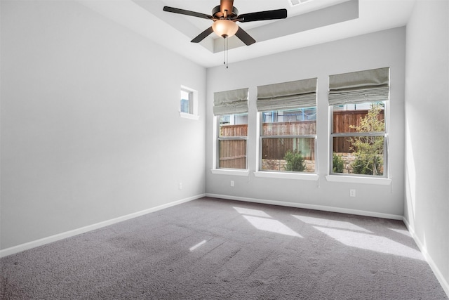 spare room with a tray ceiling, carpet flooring, baseboards, and ceiling fan