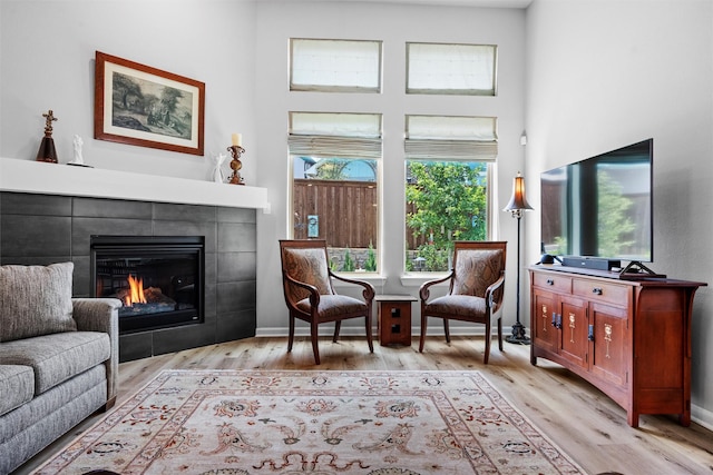 living area with a tiled fireplace, a high ceiling, and light wood-type flooring