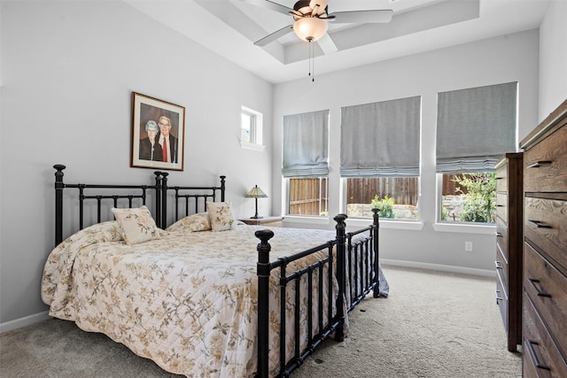 carpeted bedroom with ceiling fan, a raised ceiling, and multiple windows