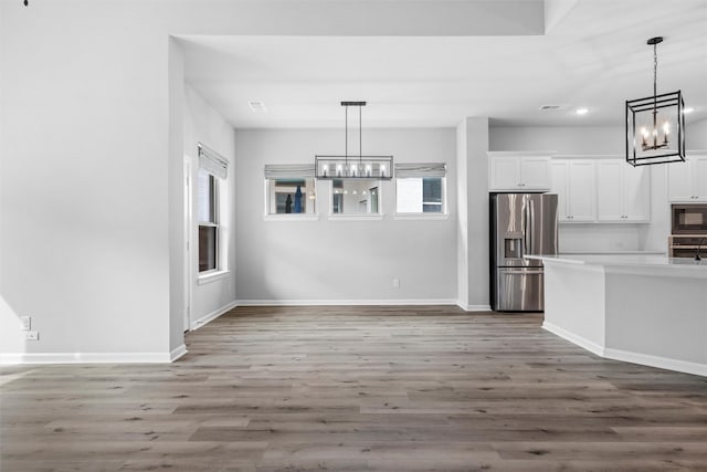 kitchen with wood finished floors, stainless steel appliances, white cabinets, a notable chandelier, and a wealth of natural light