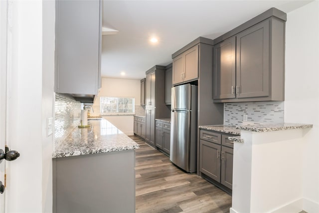 kitchen featuring gray cabinets, hardwood / wood-style flooring, stainless steel fridge, and light stone counters