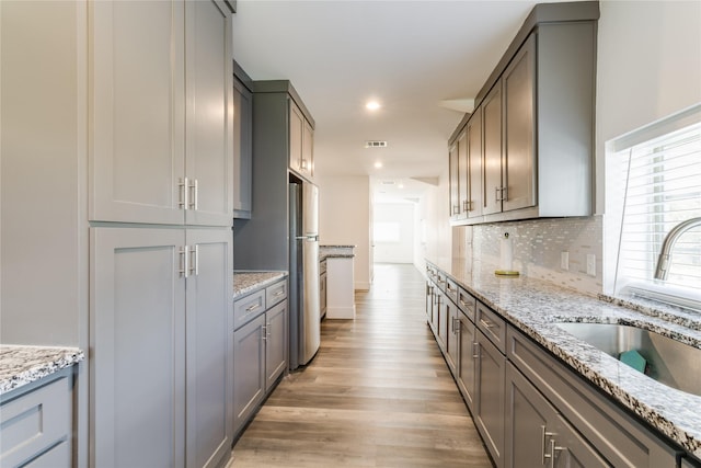 kitchen with stainless steel refrigerator, sink, decorative backsplash, light stone counters, and light hardwood / wood-style flooring