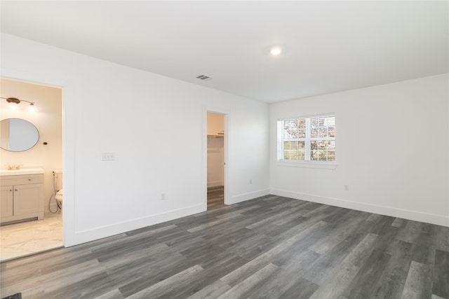 unfurnished bedroom featuring sink, ensuite bath, dark wood-type flooring, a walk in closet, and a closet