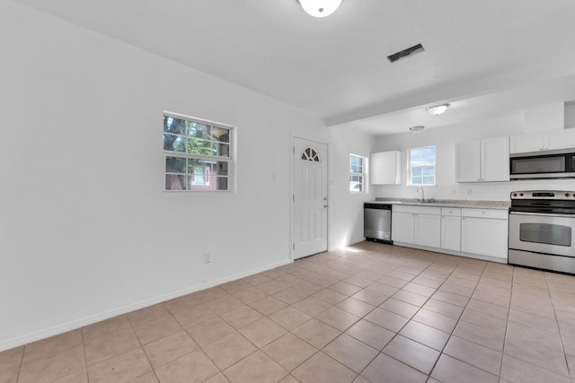 kitchen featuring appliances with stainless steel finishes, a wealth of natural light, sink, light tile patterned floors, and white cabinetry