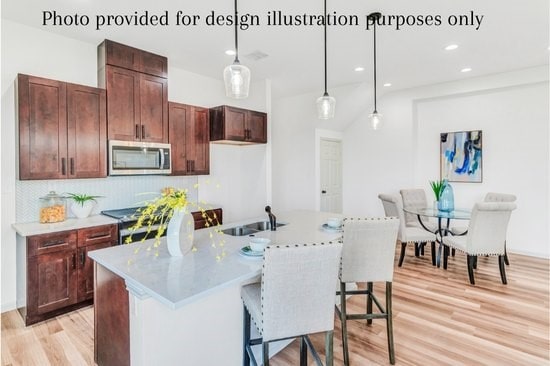 kitchen featuring decorative light fixtures, sink, stove, a center island with sink, and light hardwood / wood-style flooring