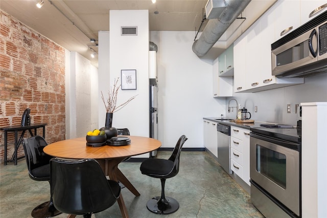 kitchen with sink, appliances with stainless steel finishes, brick wall, and white cabinetry