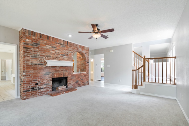 unfurnished living room with a fireplace, ceiling fan, brick wall, light colored carpet, and a textured ceiling