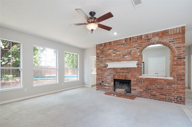 unfurnished living room with a fireplace, light colored carpet, brick wall, and ceiling fan