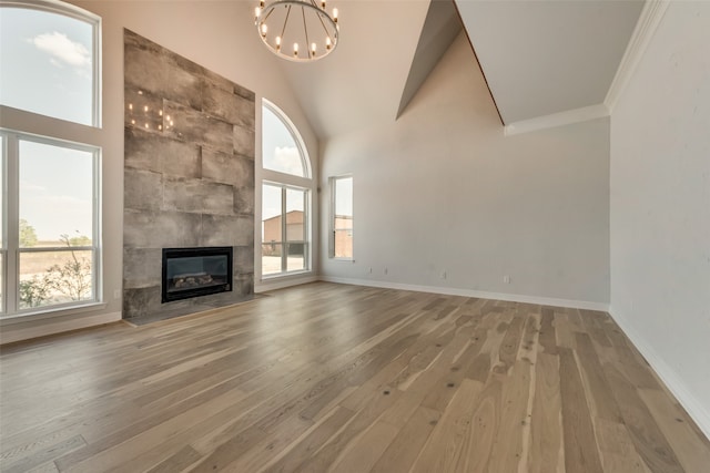 unfurnished living room with a notable chandelier, a fireplace, wood-type flooring, and high vaulted ceiling