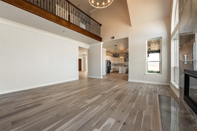 unfurnished living room featuring wood-type flooring, a towering ceiling, and a chandelier