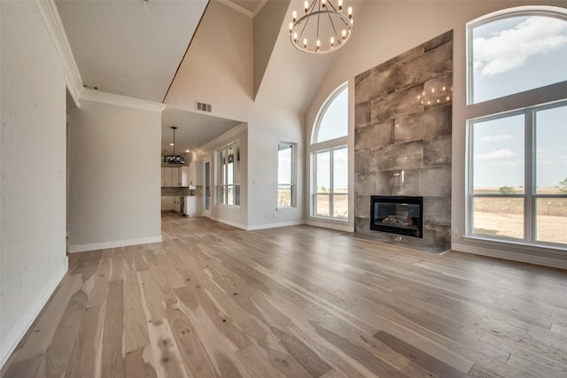 unfurnished living room with an inviting chandelier, high vaulted ceiling, a tiled fireplace, and light wood-type flooring