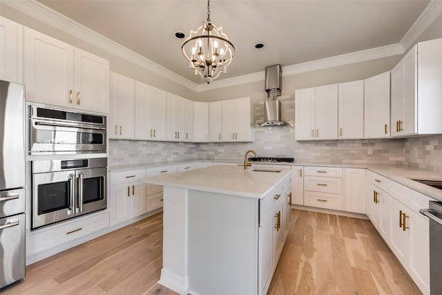 kitchen with stainless steel appliances, white cabinets, decorative backsplash, an island with sink, and light hardwood / wood-style flooring