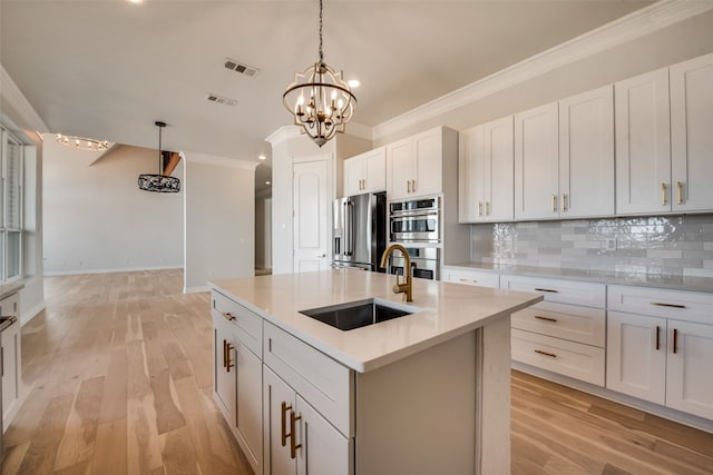 kitchen featuring light hardwood / wood-style flooring, backsplash, a kitchen island with sink, stainless steel appliances, and sink