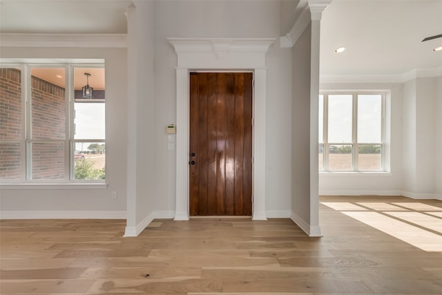 entryway with ornamental molding, light wood-type flooring, and a healthy amount of sunlight