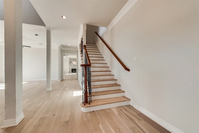 stairway featuring light hardwood / wood-style floors, ornate columns, and crown molding