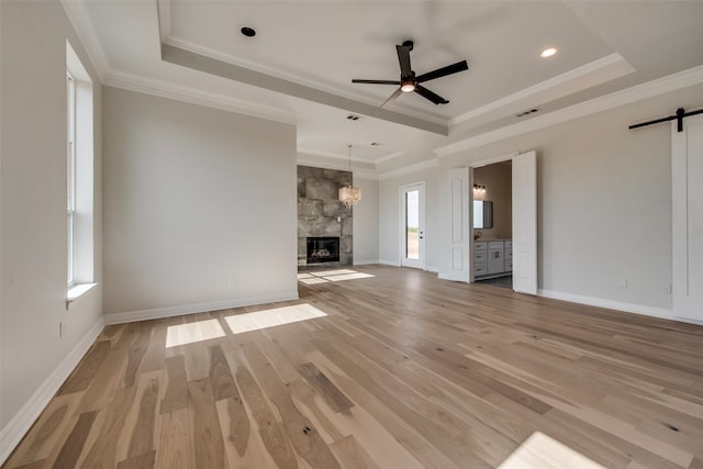 unfurnished living room featuring a barn door, ceiling fan, hardwood / wood-style floors, a stone fireplace, and a raised ceiling