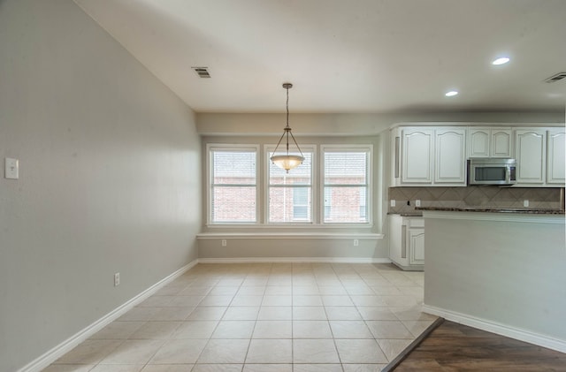 kitchen featuring backsplash, white cabinetry, light tile patterned floors, and decorative light fixtures