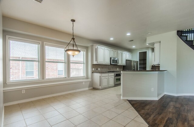 kitchen featuring kitchen peninsula, tasteful backsplash, stainless steel appliances, light tile patterned floors, and white cabinets