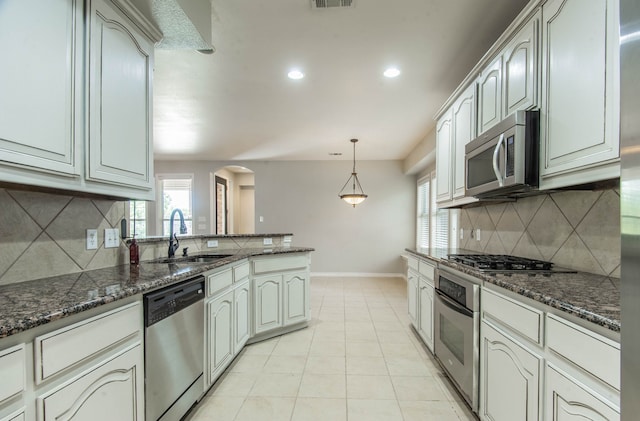 kitchen with sink, light tile patterned floors, stainless steel appliances, and dark stone counters