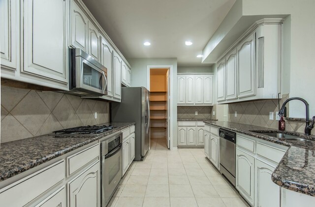 kitchen with dark stone counters, sink, appliances with stainless steel finishes, light tile patterned flooring, and white cabinetry