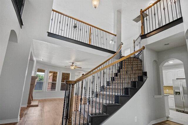 stairway with a towering ceiling, hardwood / wood-style flooring, and ceiling fan