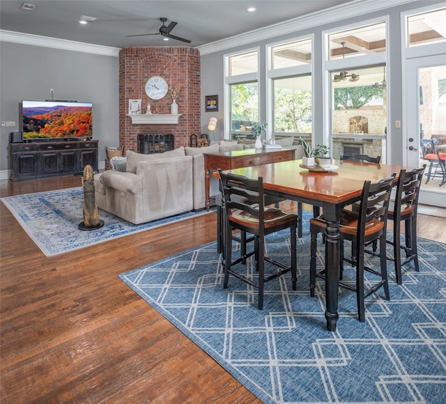 dining area featuring ceiling fan, crown molding, dark hardwood / wood-style floors, and a brick fireplace