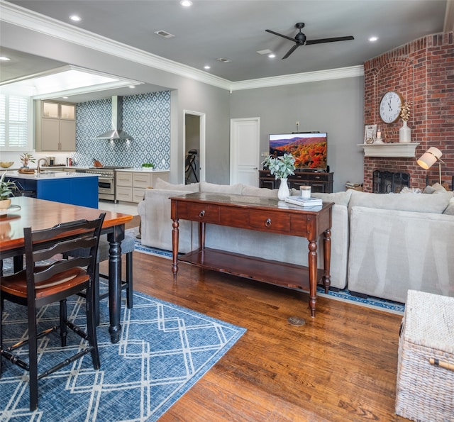 dining space featuring ceiling fan, ornamental molding, dark wood-type flooring, and a brick fireplace