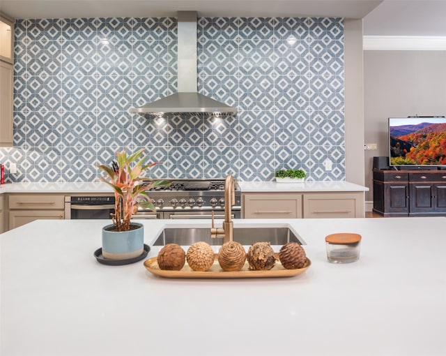 kitchen with cream cabinets, sink, crown molding, and wall chimney range hood