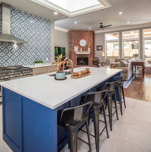 kitchen featuring high end stainless steel range oven, wall chimney exhaust hood, ceiling fan, light wood-type flooring, and ornamental molding