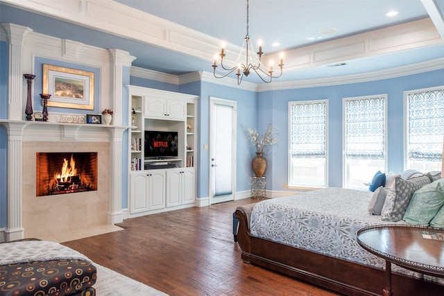 bedroom featuring a tiled fireplace, an inviting chandelier, wood-type flooring, and ornamental molding