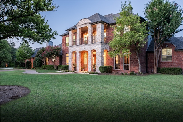 view of front of property with stone siding, brick siding, a balcony, and a front lawn