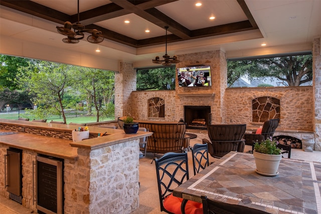 view of patio featuring an outdoor stone fireplace, an outdoor bar, ceiling fan, and beverage cooler