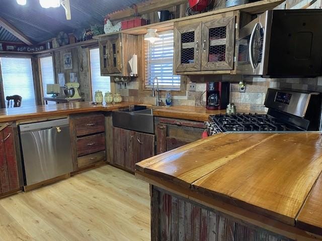 kitchen featuring backsplash, sink, vaulted ceiling, light wood-type flooring, and stainless steel appliances