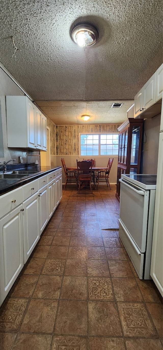 kitchen with white cabinetry, a textured ceiling, dark tile patterned flooring, and white range with electric stovetop