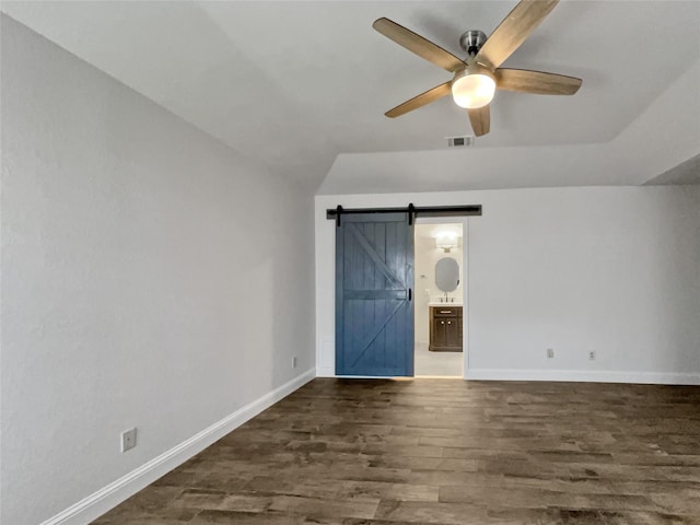 unfurnished bedroom with ensuite bath, lofted ceiling, ceiling fan, a barn door, and dark hardwood / wood-style flooring