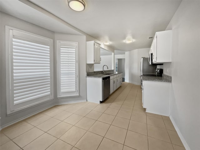 kitchen with appliances with stainless steel finishes, dark stone counters, sink, white cabinetry, and light tile patterned flooring