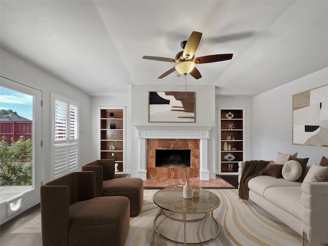 living room with ceiling fan, a premium fireplace, built in features, and light wood-type flooring