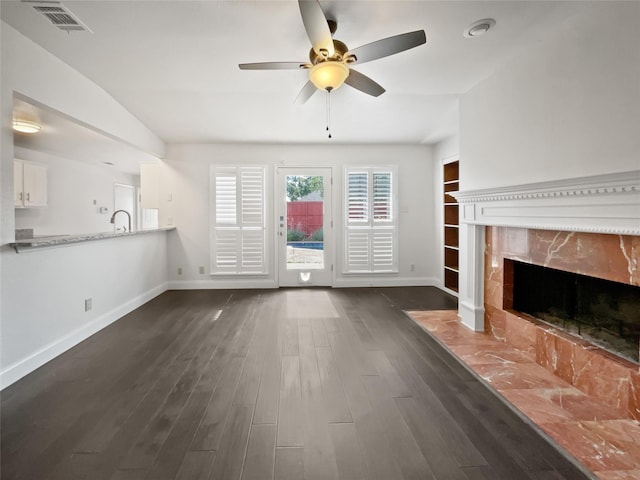 unfurnished living room featuring sink, lofted ceiling, ceiling fan, a high end fireplace, and dark wood-type flooring