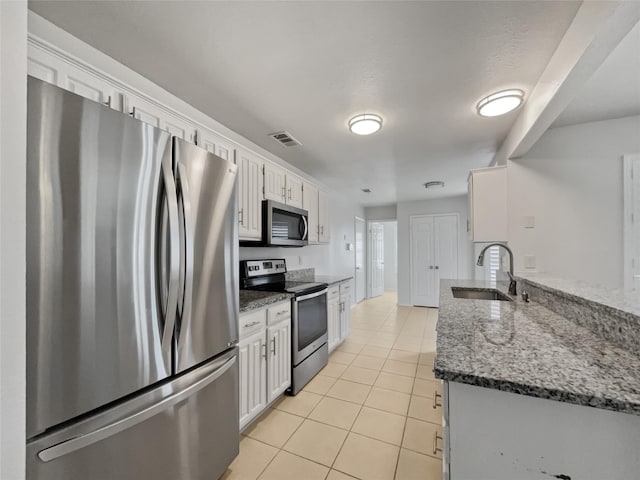 kitchen with light tile patterned floors, white cabinetry, dark stone counters, appliances with stainless steel finishes, and sink