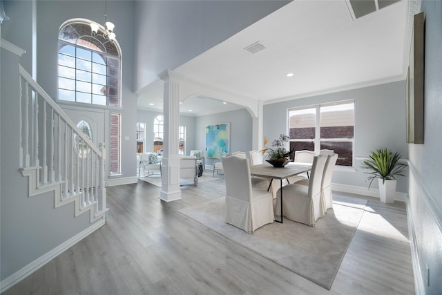 dining room with a towering ceiling, light wood-type flooring, decorative columns, crown molding, and a notable chandelier