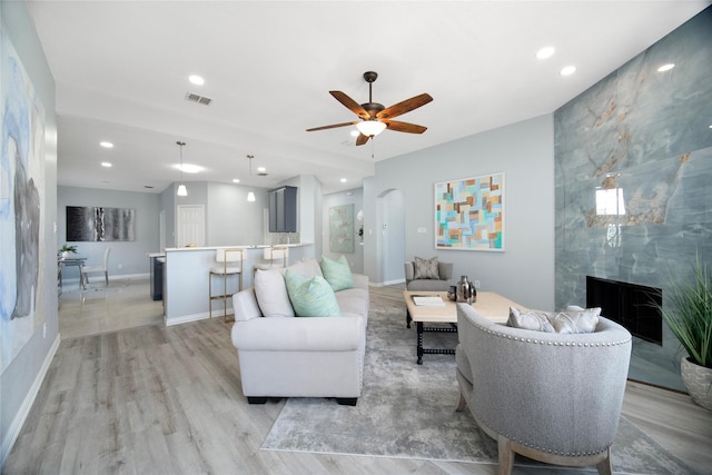 living room with light wood-type flooring, ceiling fan, and a premium fireplace