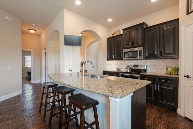 kitchen featuring sink, a breakfast bar area, an island with sink, stainless steel appliances, and backsplash