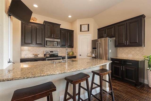 kitchen with sink, light stone countertops, a breakfast bar, and appliances with stainless steel finishes